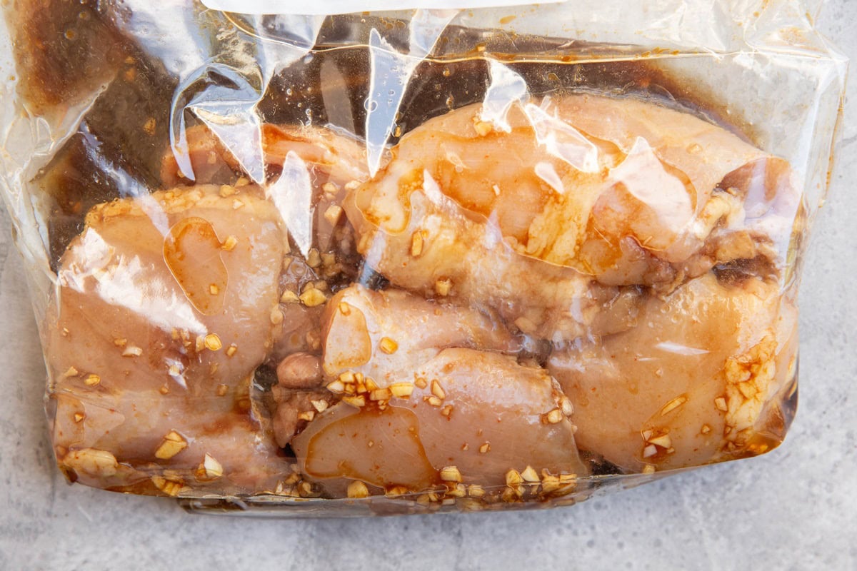 Chicken thighs marinating in a large plastic bag for sheet pan chicken.