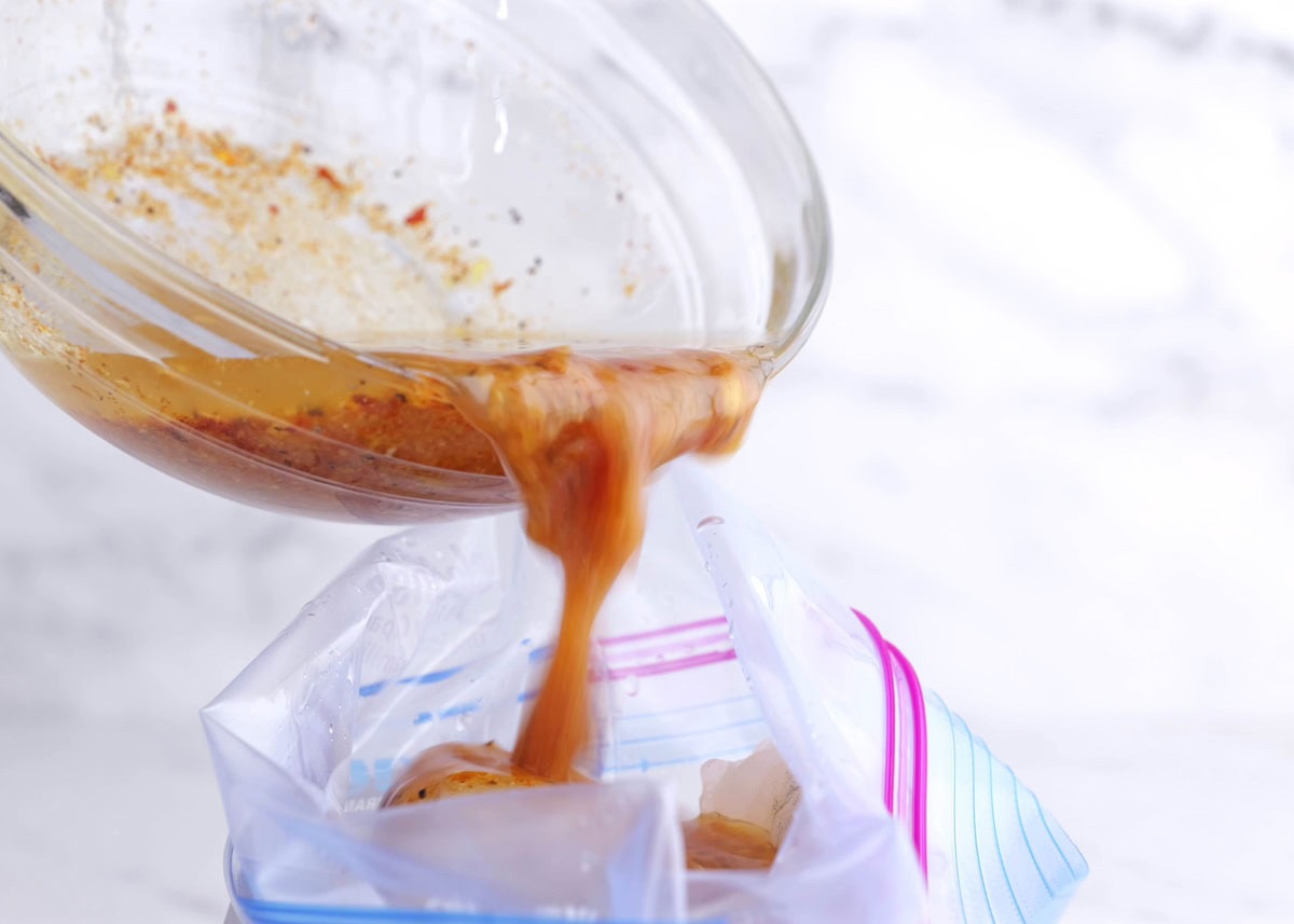 Pouring marinade into a zip lock bag with raw shrimp.