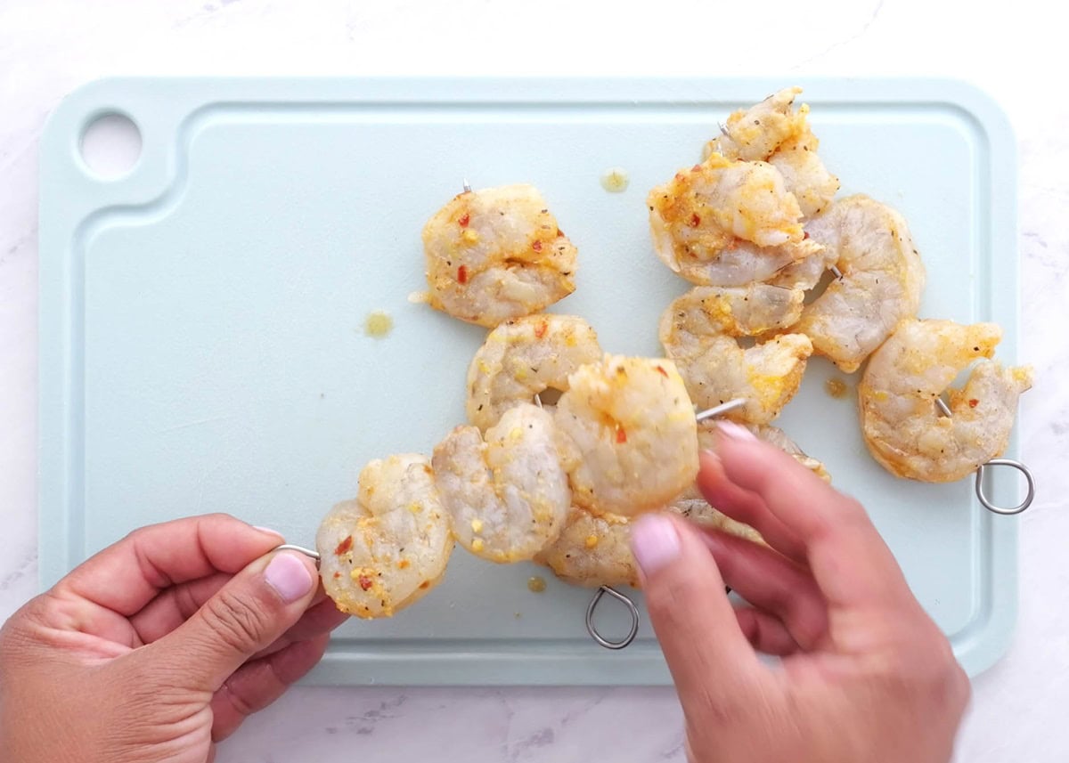 Threading the marinated shrimp onto skewers to make shrimp kebabs.