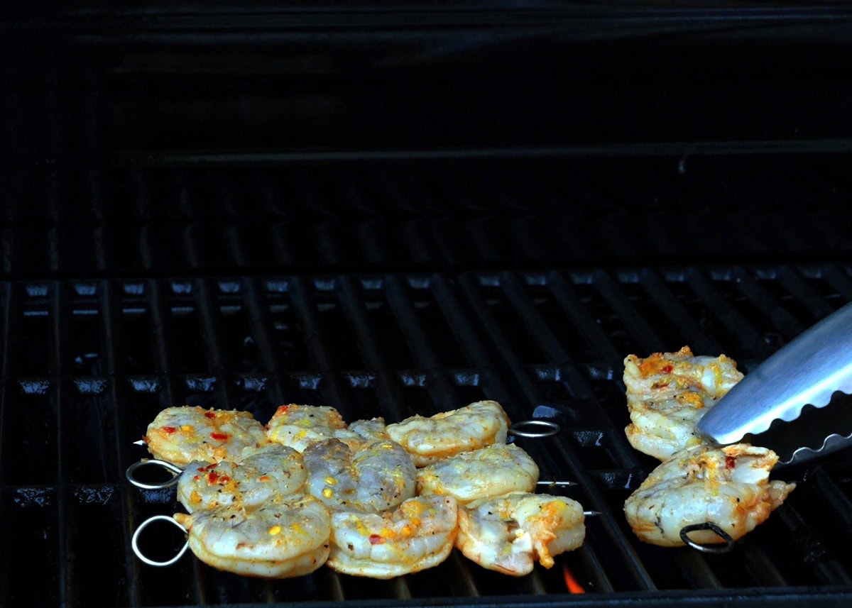 Tongs placing shrimp kebabs on a hot grill.