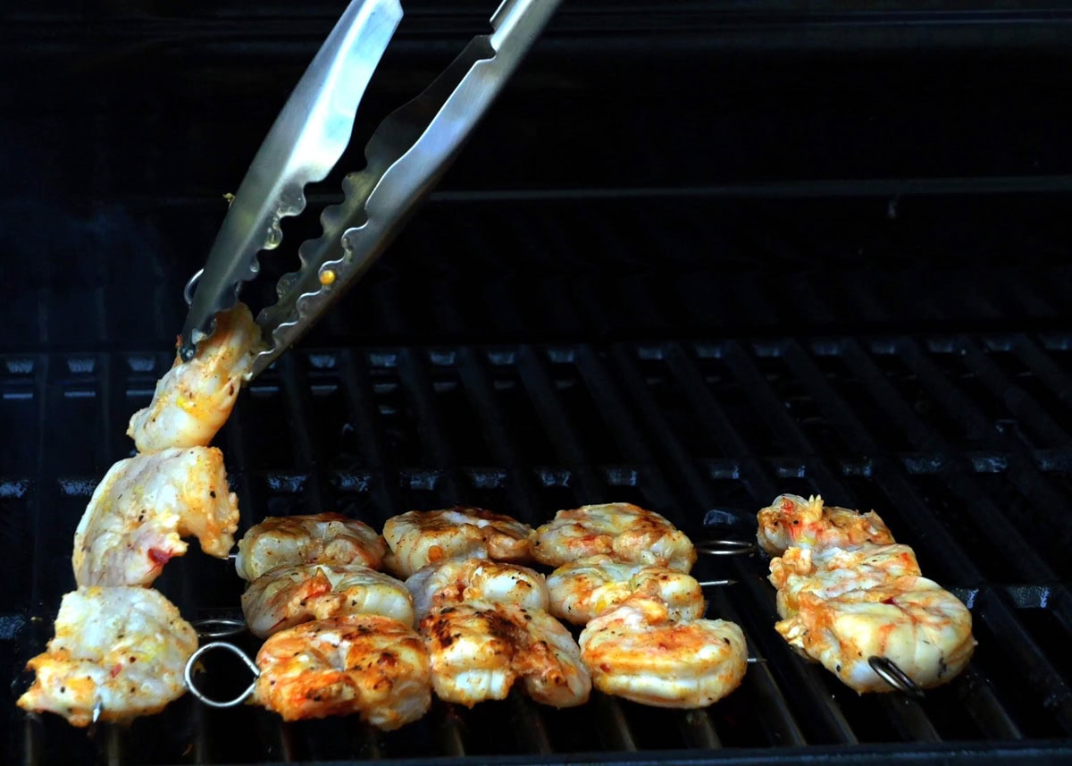 Shrimp grilling on an outdoor grill, being flipped by tongs.