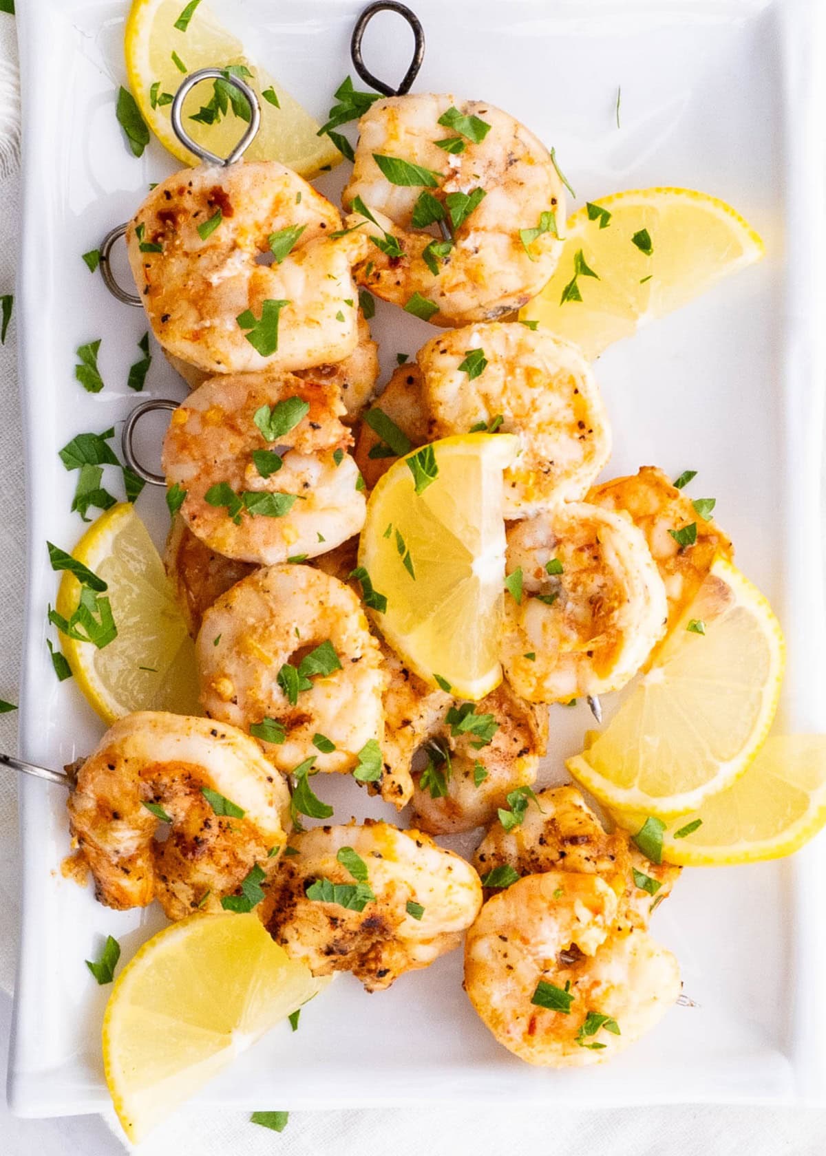 Platter of grilled shrimp skewers ready to serve with fresh lemon slices.