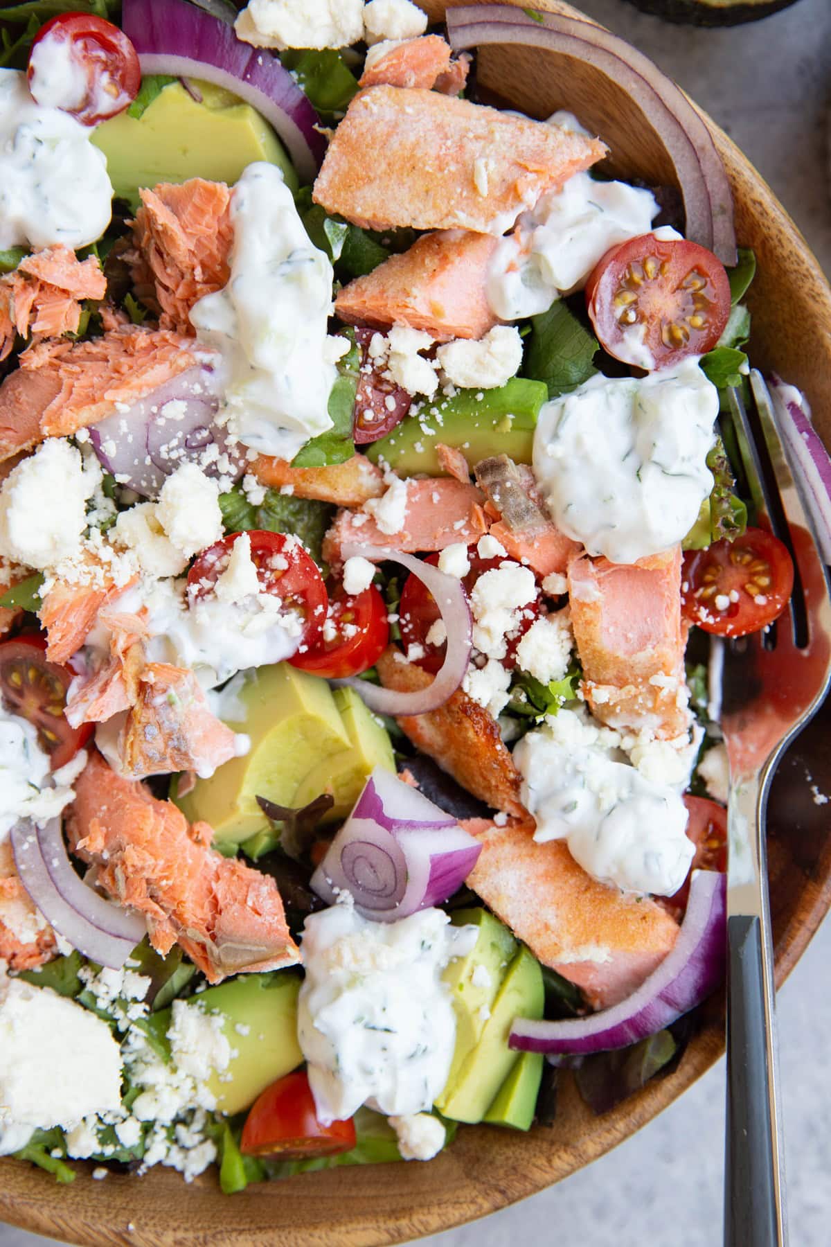 salmon salad in a wooden bowl with tzatziki sauce and avocado.