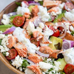 Big bowl of salmon salad with avocado in the background.