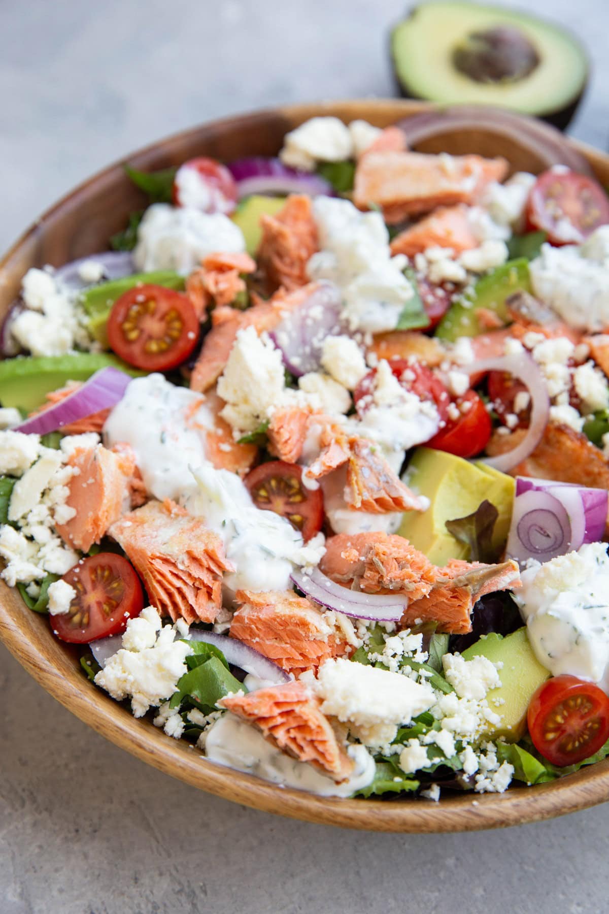 Big bowl of salmon salad with avocado in the background.