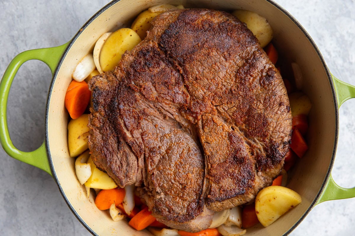 Large pot of vegetables with a seared beef roast on top to make oven-baked pot roast.