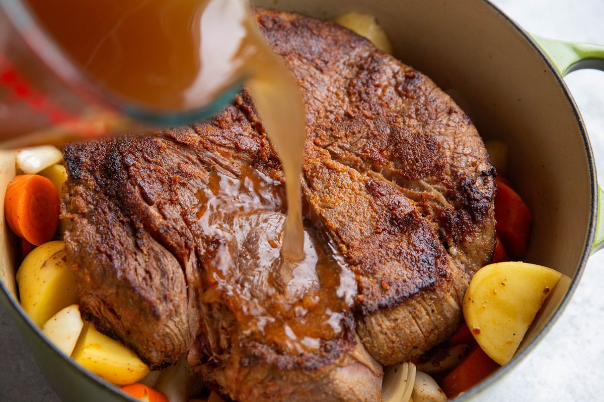 Pouring broth into the pot with the beef and veggies.