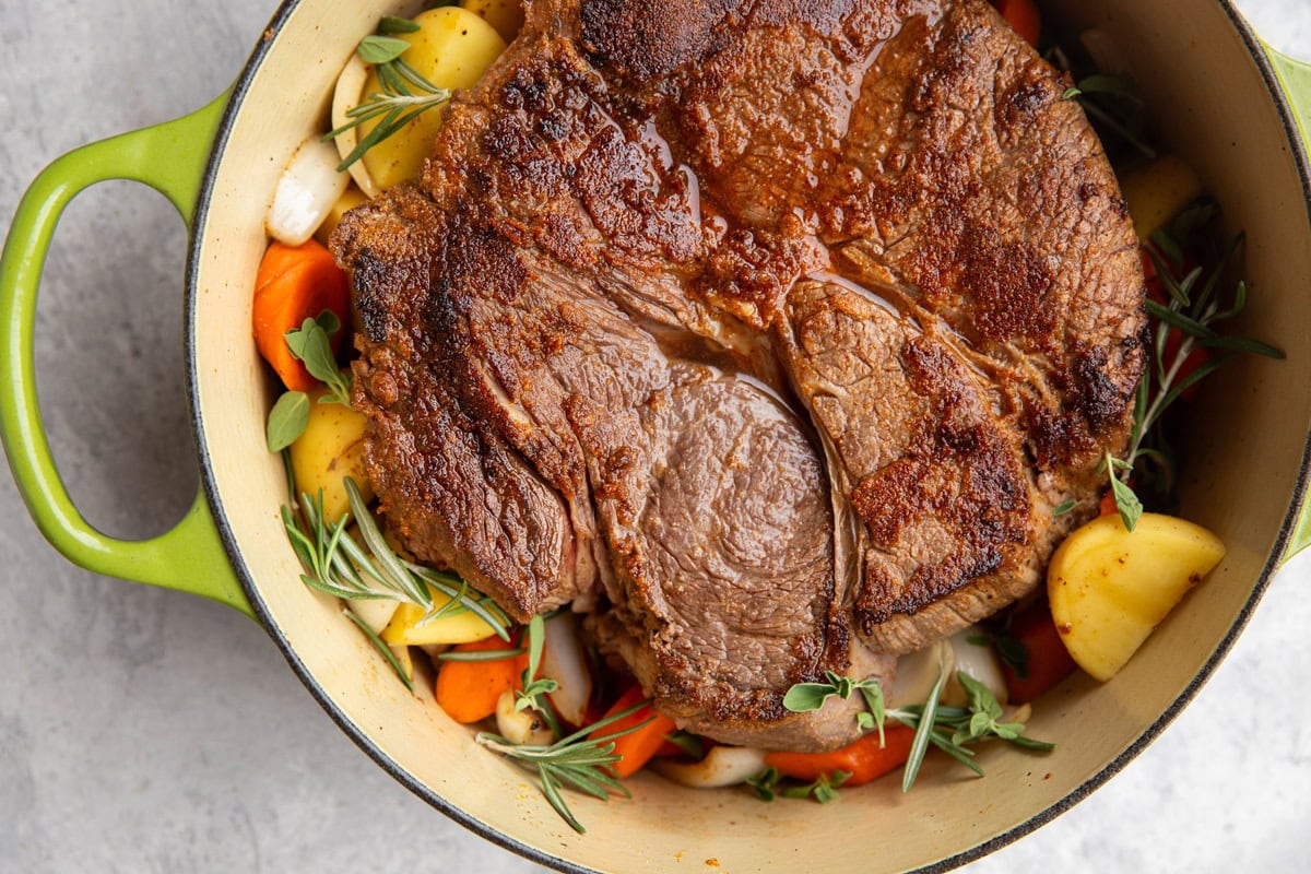 Beef roast in a pot with vegetables and herbs, ready to go into the oven.