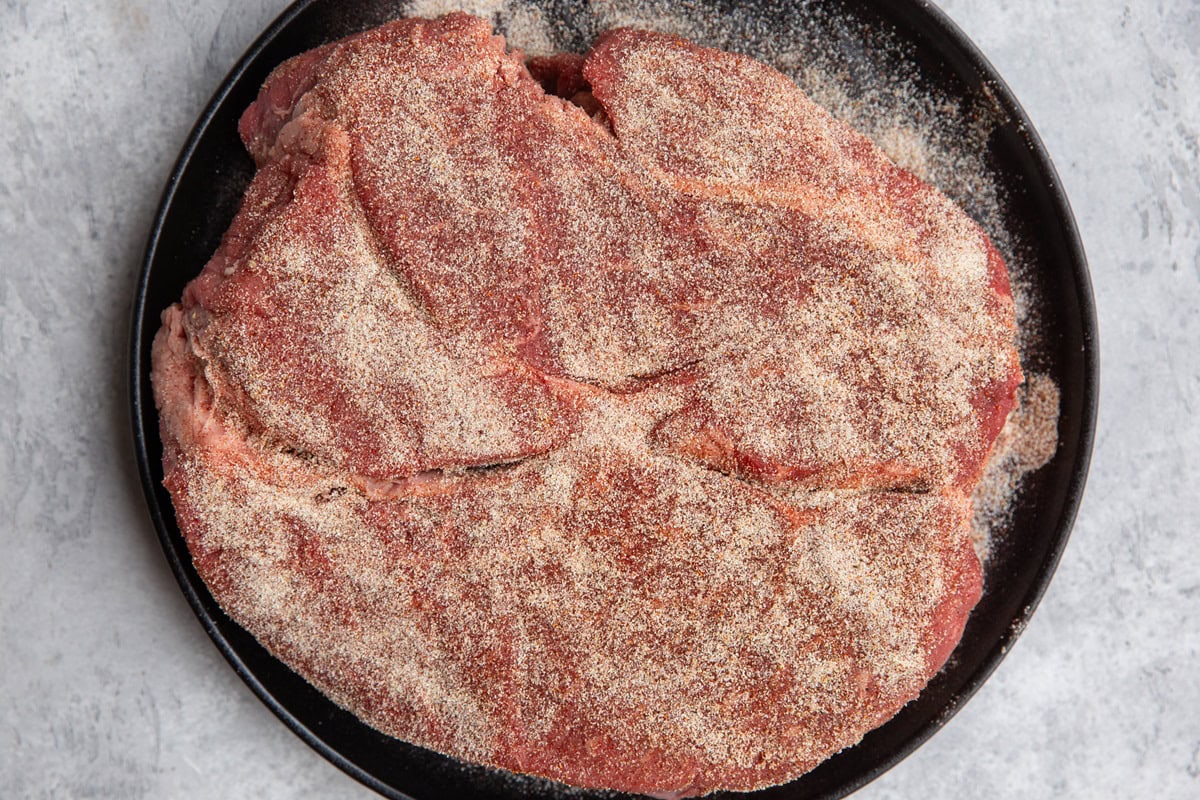 large beef roast on a plate sprinkled with seasonings.