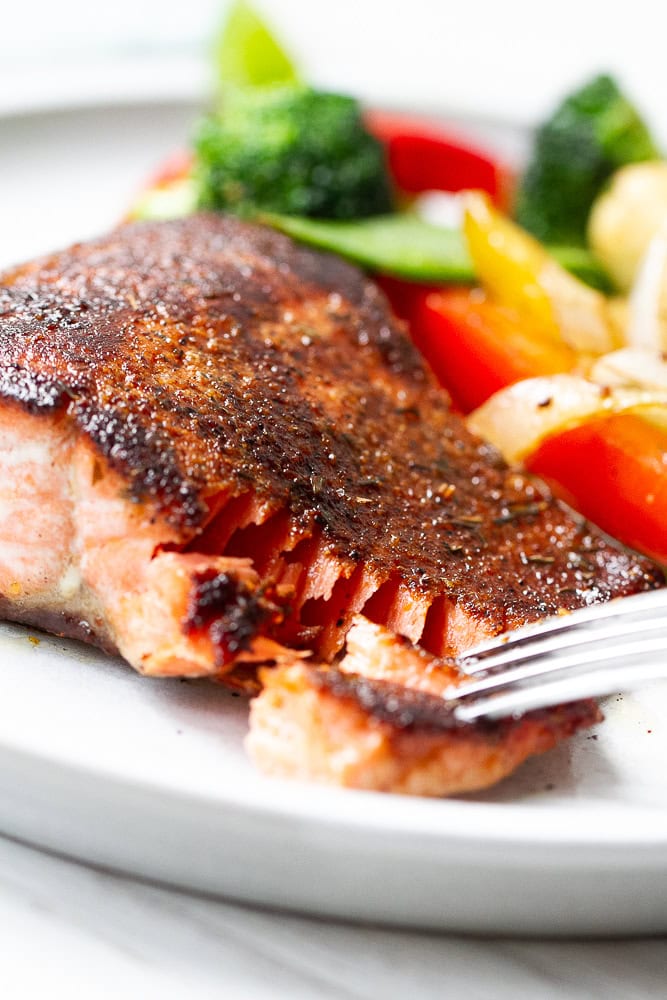 Blackened salmon on a white plate with a bite taken out.