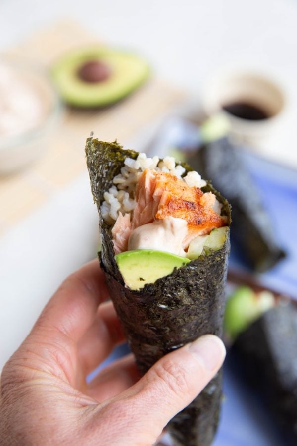 Hand holding a salmon hand roll, ready to eat.