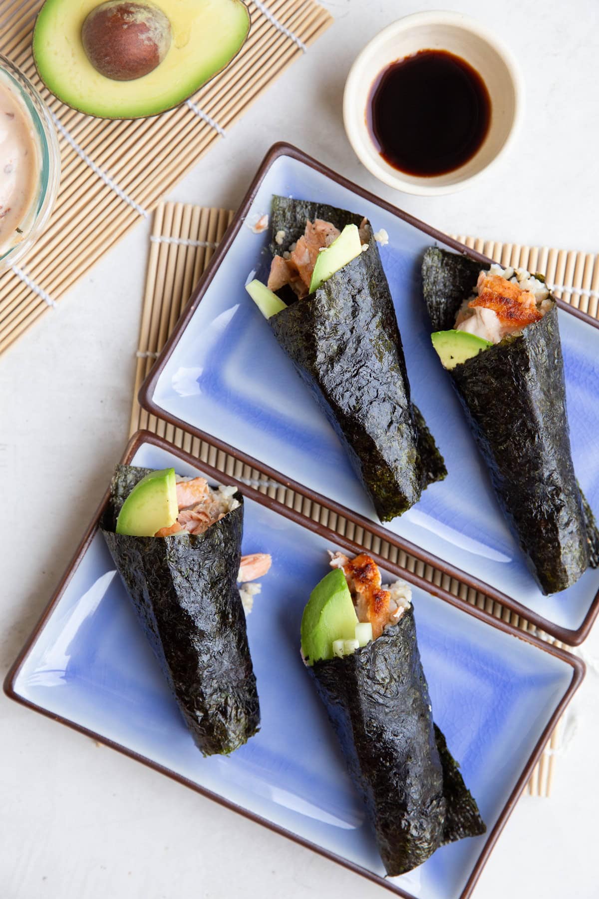 Four salmon hand rolls on plates with sauces to the side, ready to eat.