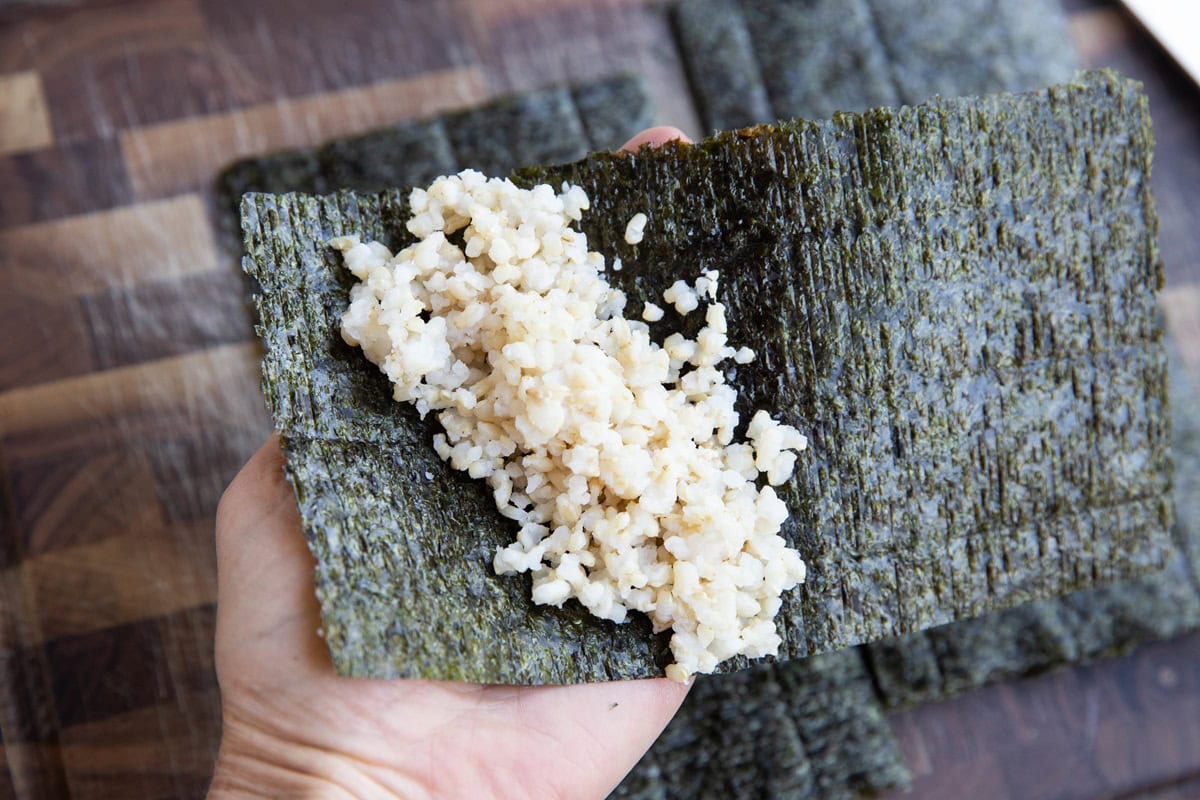 Hand holding a sheet of seaweed with rice placed in a diagonal