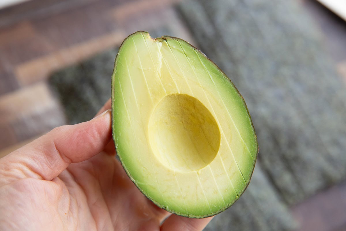 Hand holding an avocado that's cut into slices.