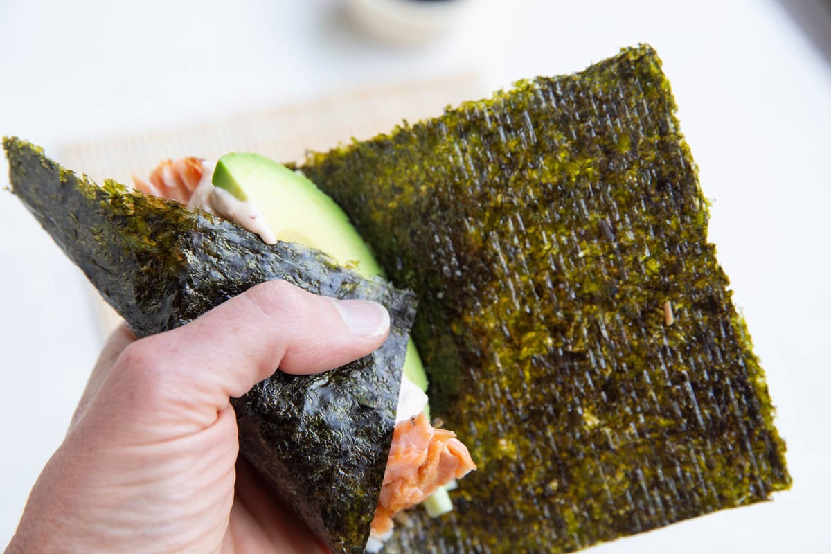 Hand holding a hand roll that is being wrapped into a cone shape.