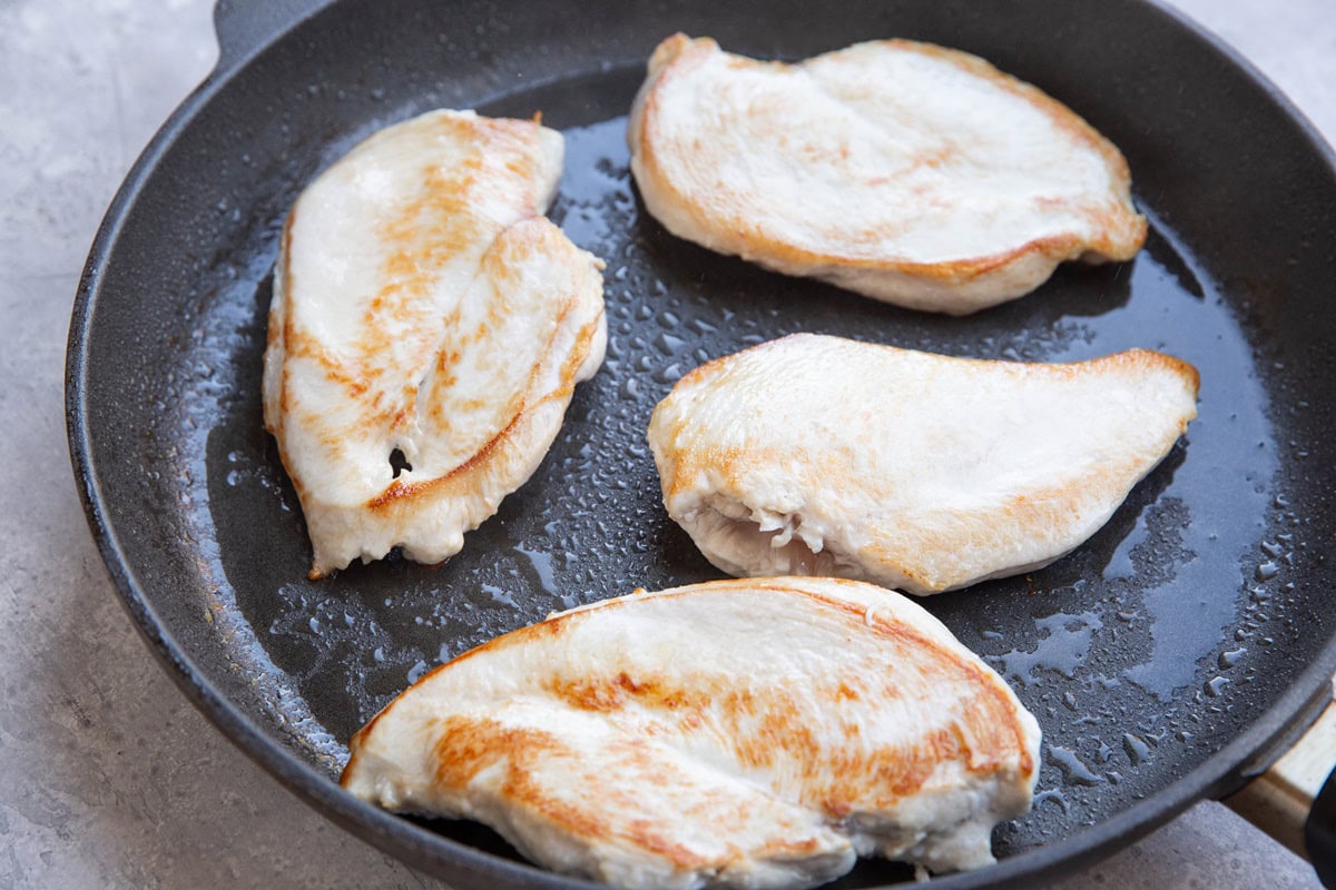 Chicken breasts being seared in a large skillet.