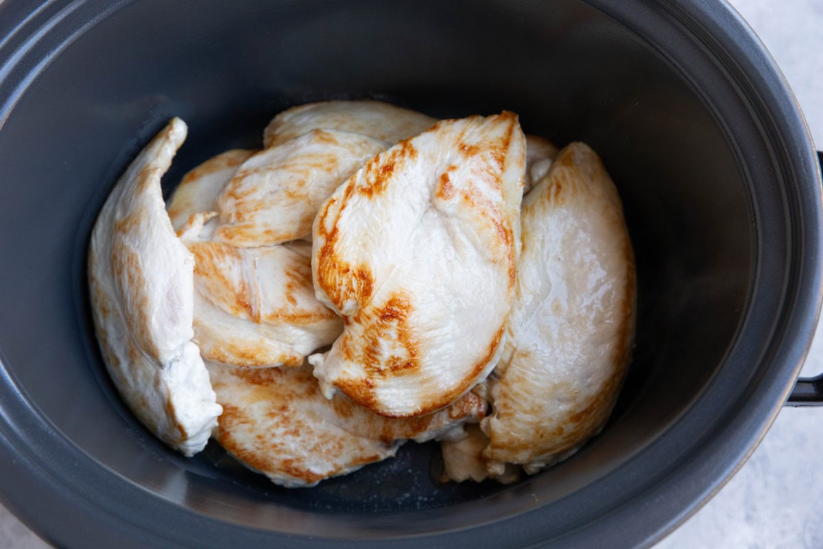 Crock pot with chicken breasts inside.