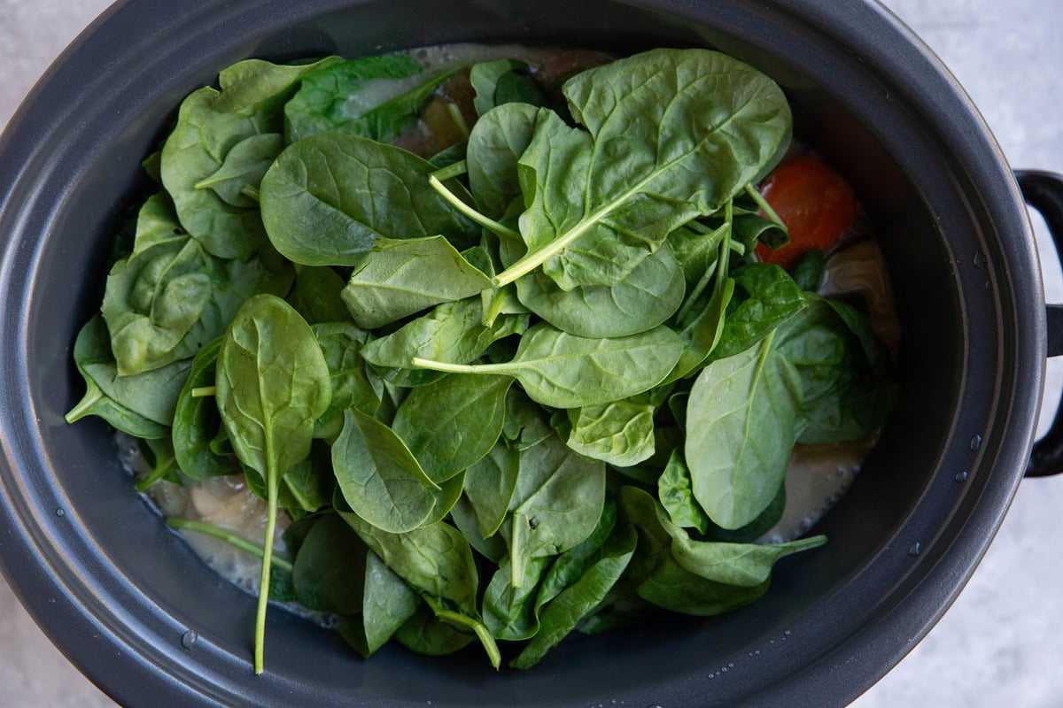 Baby spinach on top of vegetables in a slow cooker.