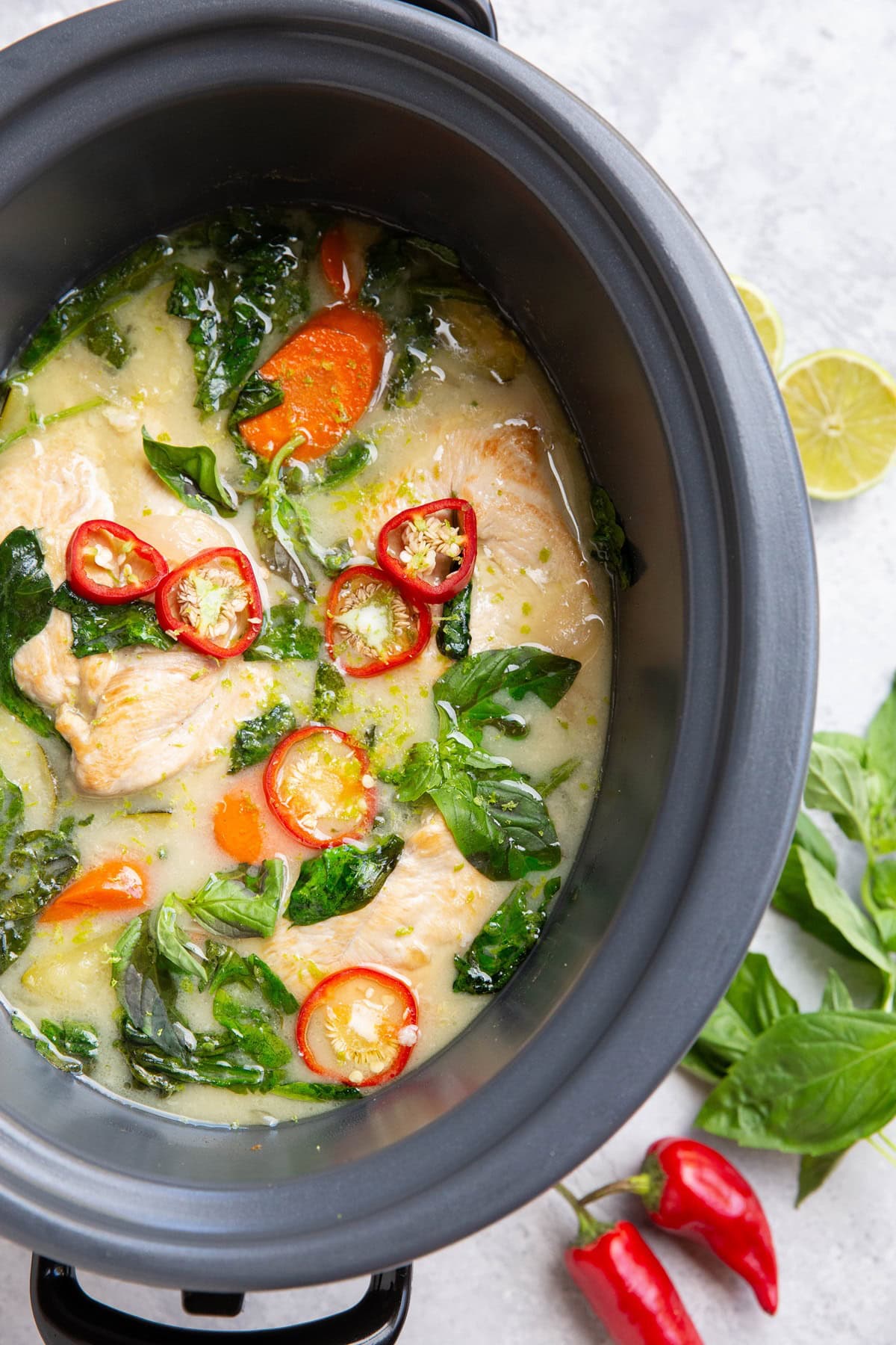 Crock pot full of chicken and sauce with basil and red chilies on top.