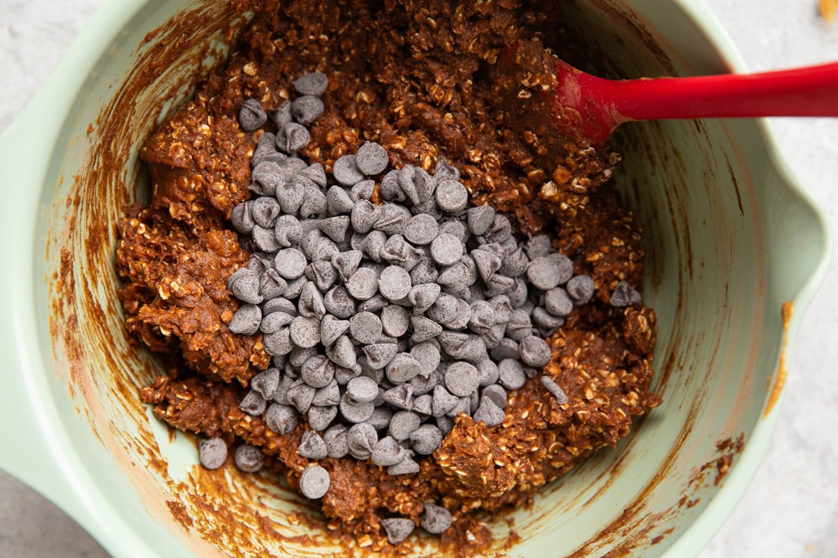 Chocolate chips on top of oatmeal cookie batter, ready to be mixed in.