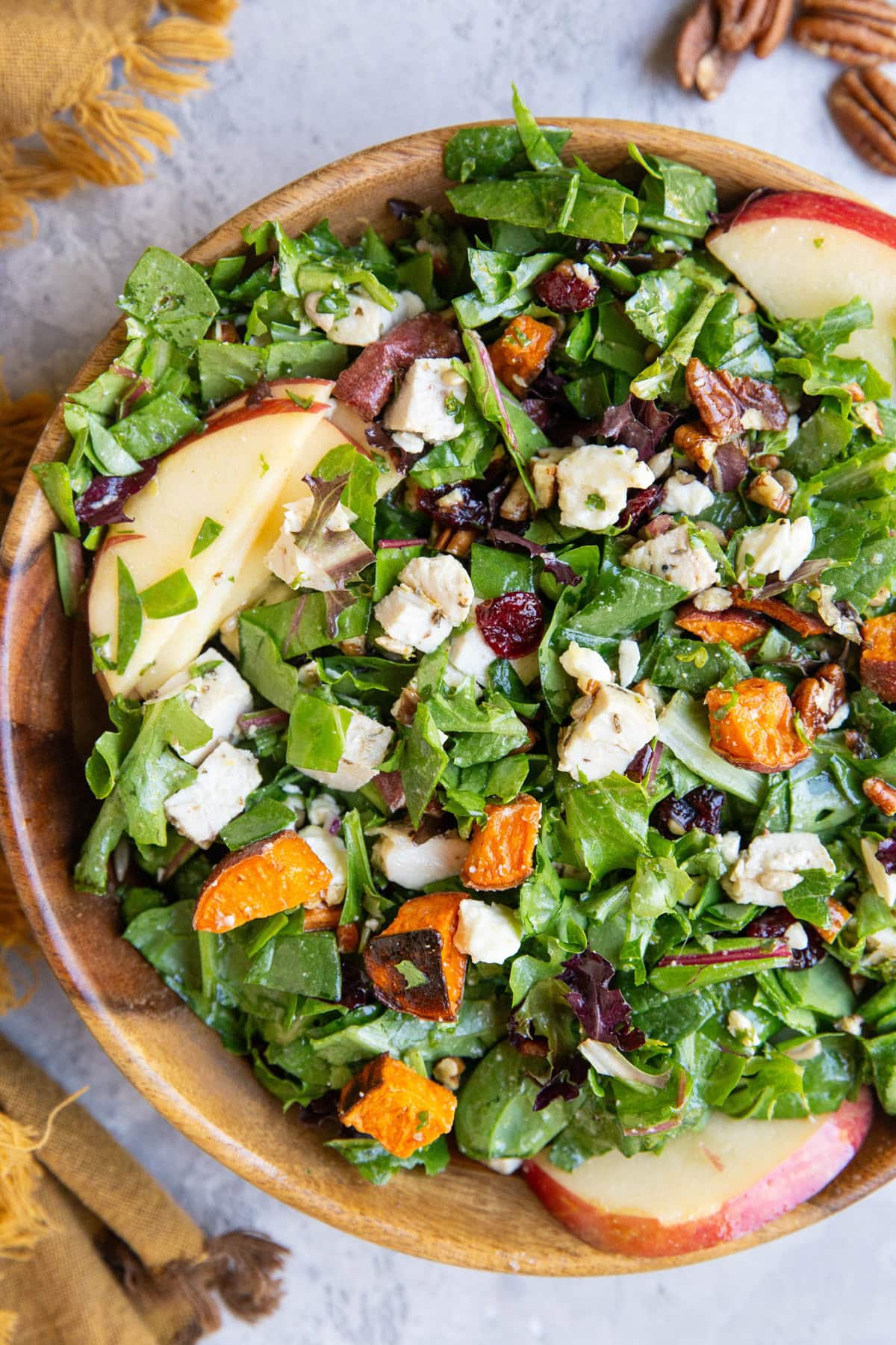 Wooden bowl of chicken and sweet potato salad with a napkin and pecans to the side.