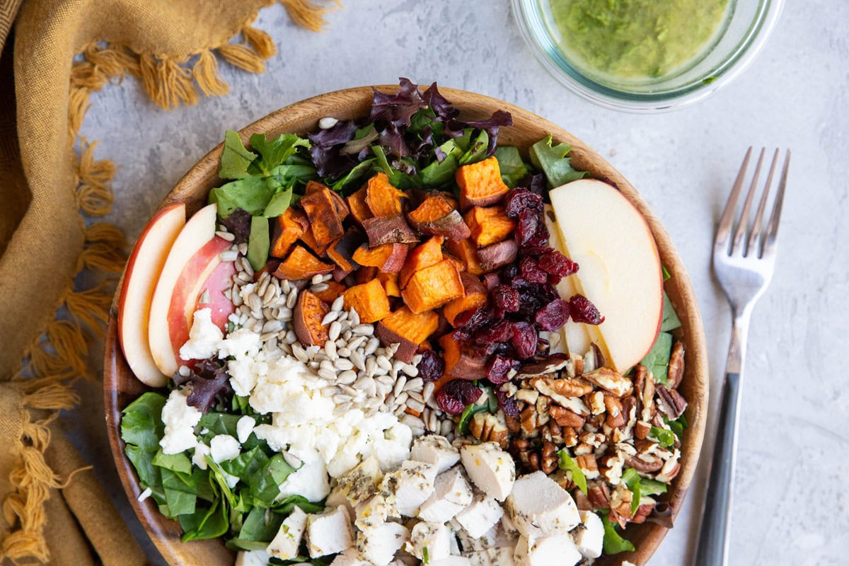 Big wooden bowl of salad with chicken, sweet potato, pecans, apples, and dried cranberries