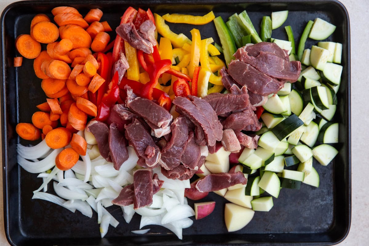 Sliced steak and chopped vegetables on a large rimmed baking sheet.