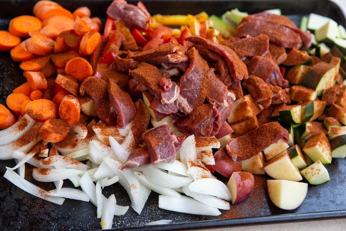 Steak and vegetables on a sheet pan with seasonings sprinkled on top.