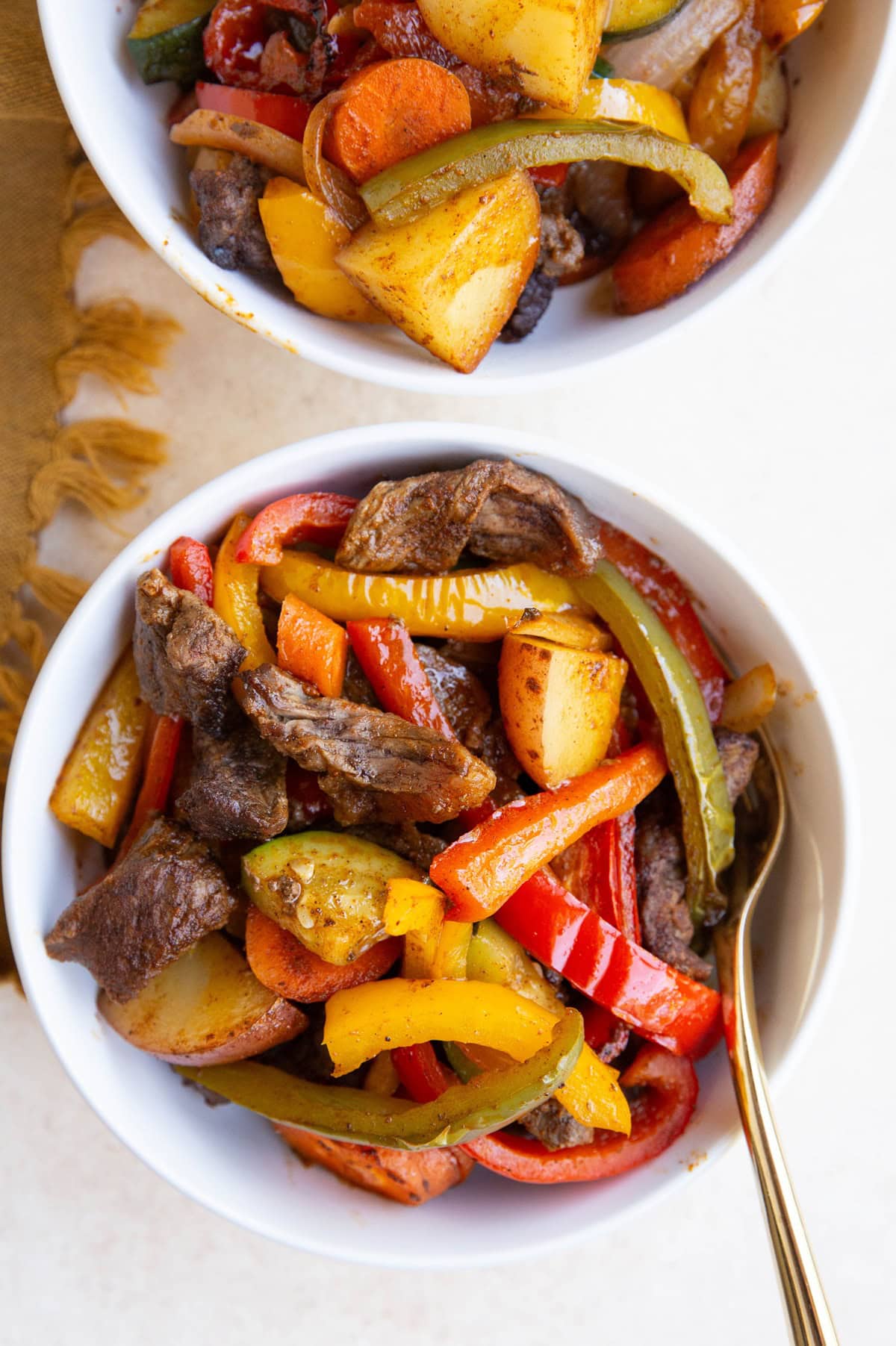 Two white bowls full of steak and vegetables.