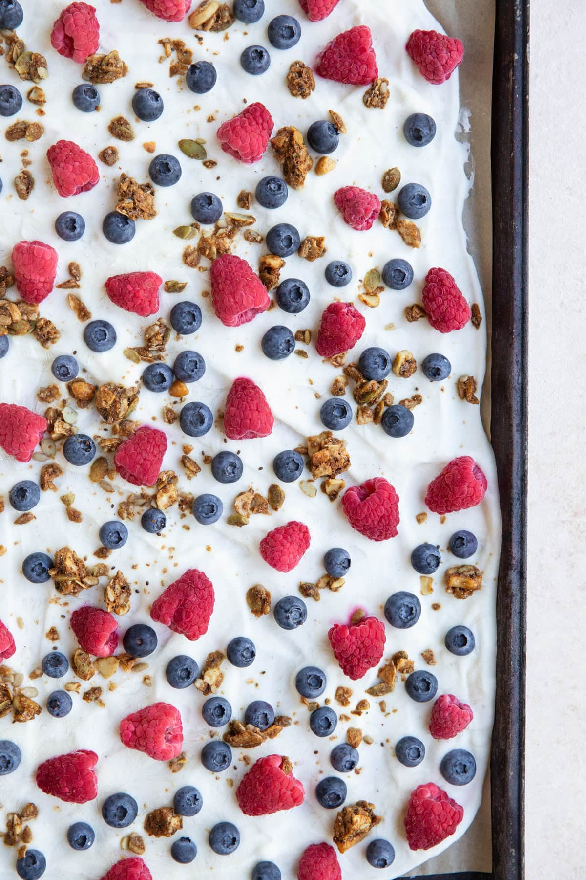 Sheet pan with yogurt, berries, and granola spread over it to make yogurt bark, ready to go into the freezer.