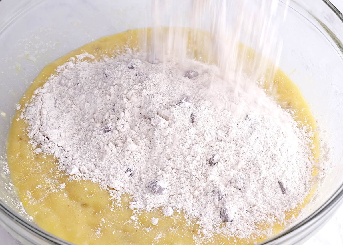 Pouring flour mixture into a bowl with the wet mixture of banana muffins.