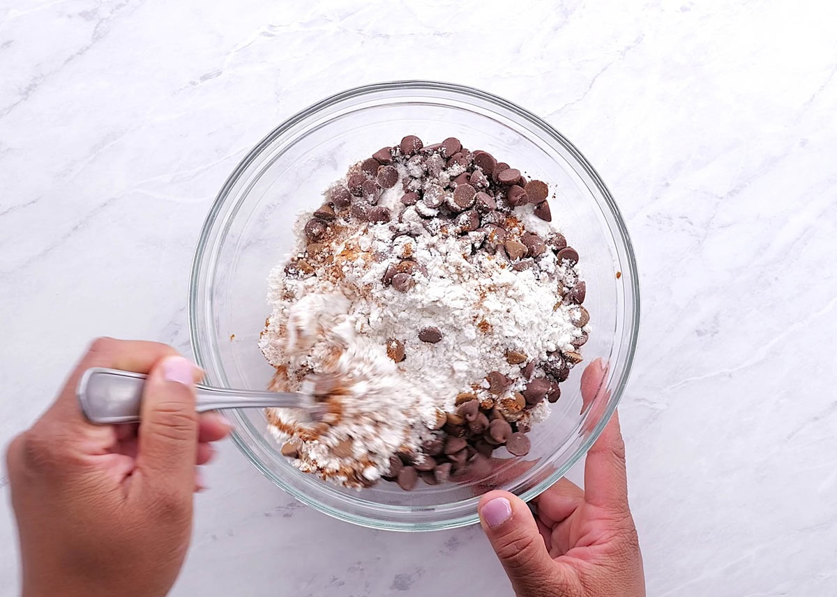 Hands mixing dry ingredients together in a mixing bowl.