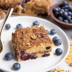 Slice of Greek yogurt coffee cake on a plate with the rest of the coffee cake in the background.