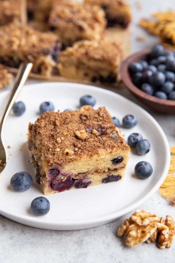 Slice of Greek yogurt coffee cake on a plate with the rest of the coffee cake in the background.