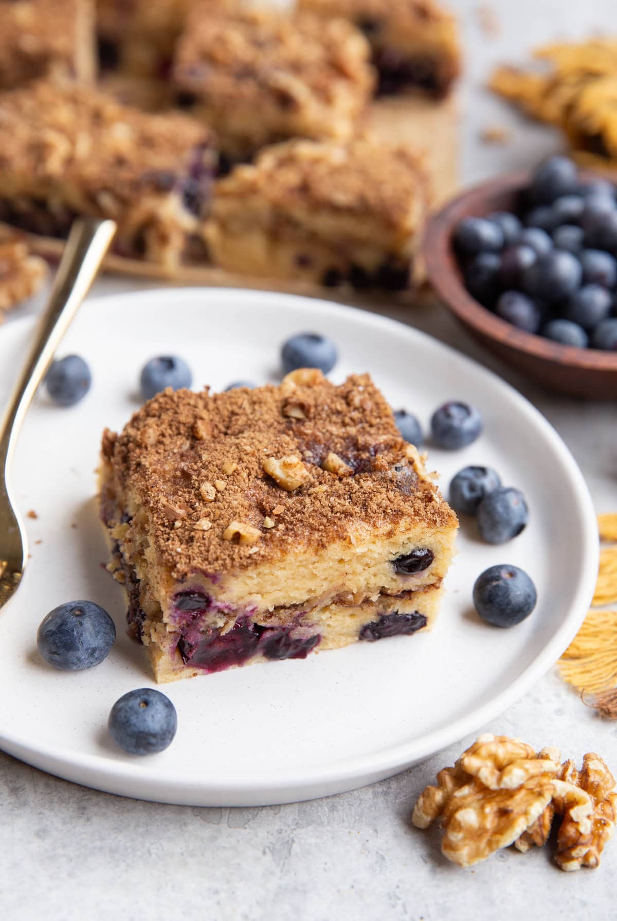 Slice of Greek yogurt coffee cake on a plate with the rest of the coffee cake in the background.