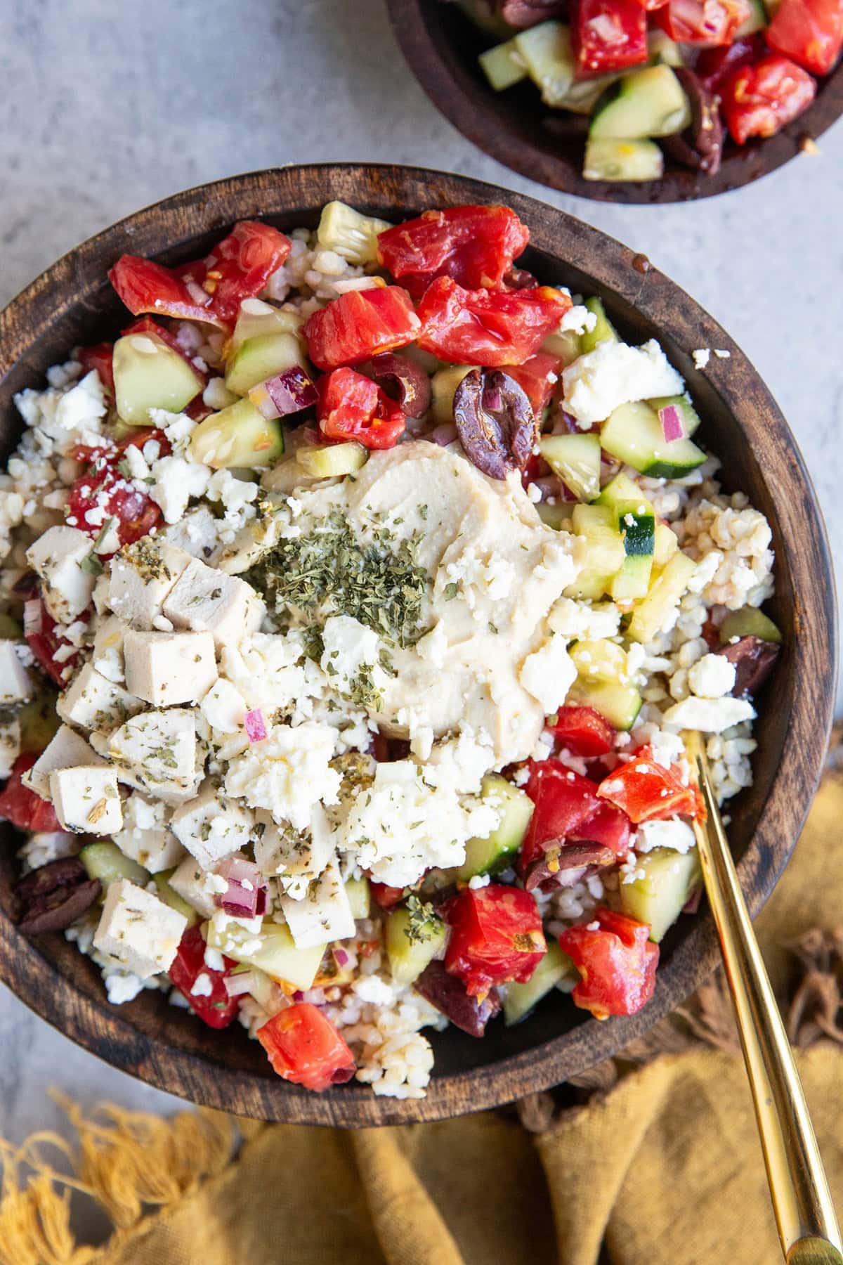 Big wooden bowl of chicken, hummus, rice, and cucumber tomato salad.