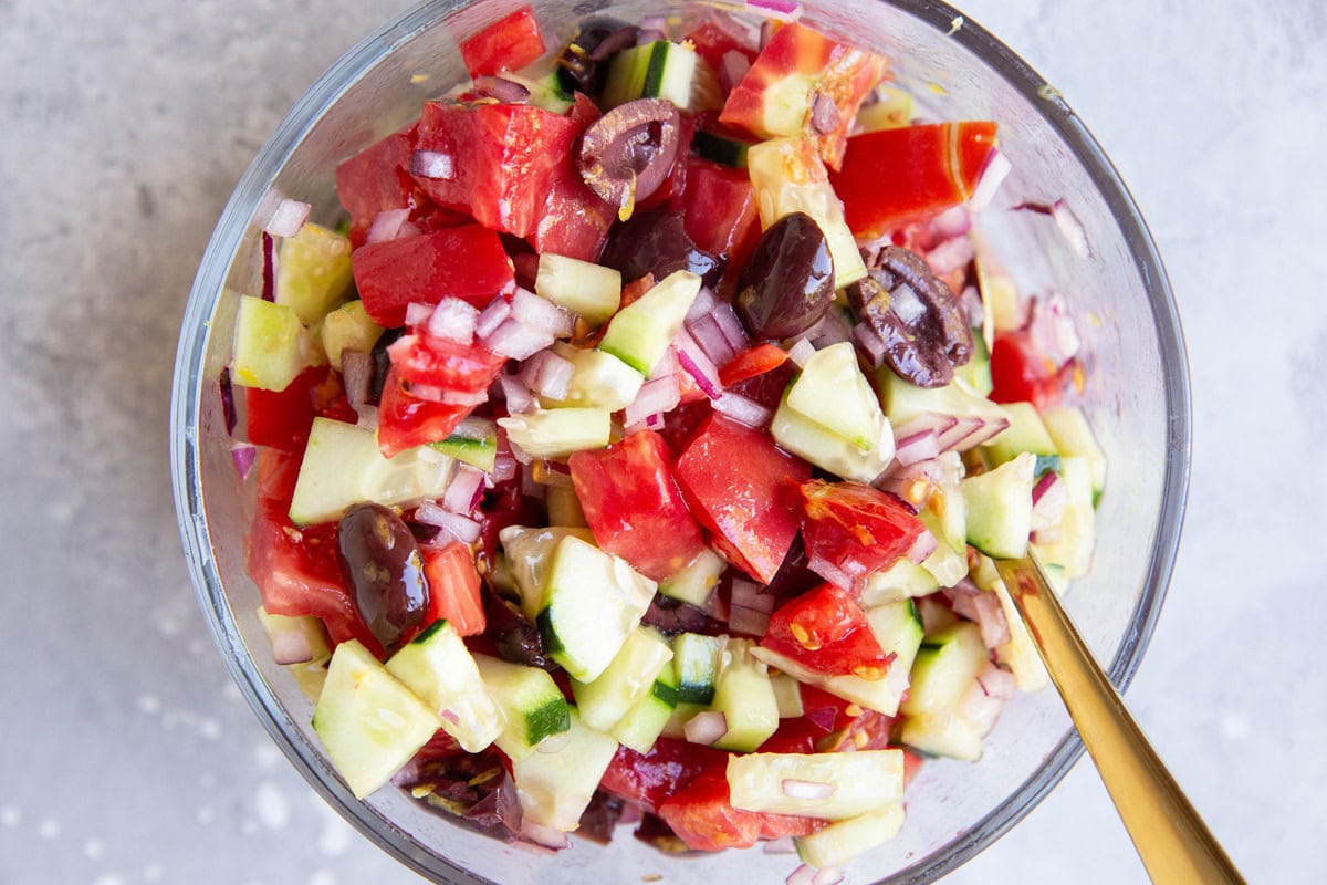 Cucumber tomato olive salad in a glass bowl.