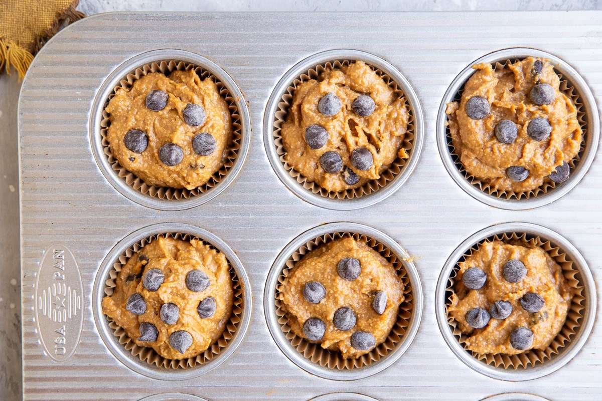 Muffin tin with pumpkin muffin batter inside, ready to bake.