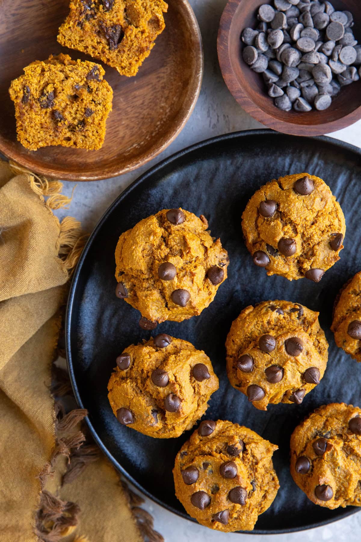 Black plate of pumpkin muffins and a wooden plate with a muffin cut in half.