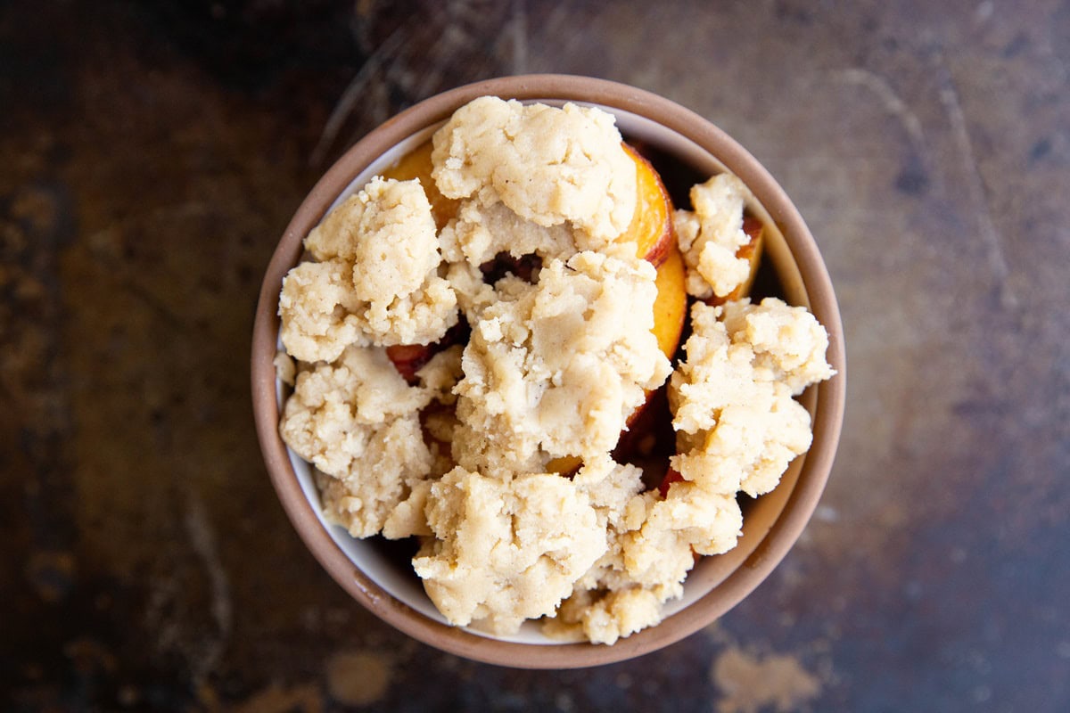 ramekin with peach filling and crumble topping, ready to go into the oven.