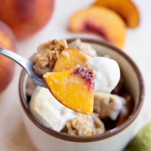 Spoon holing a scoop of peach cobbler with ice cream.