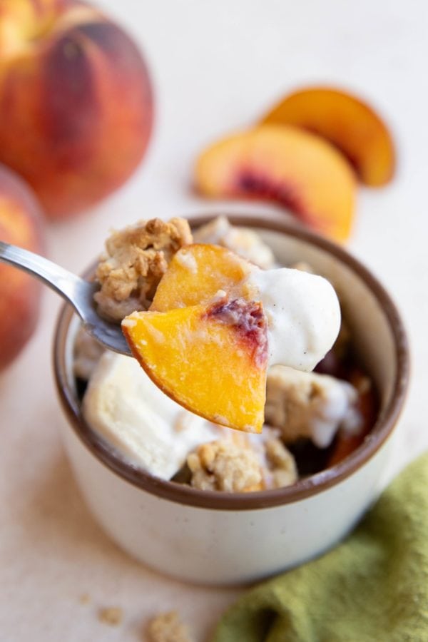 Spoon holing a scoop of peach cobbler with ice cream.