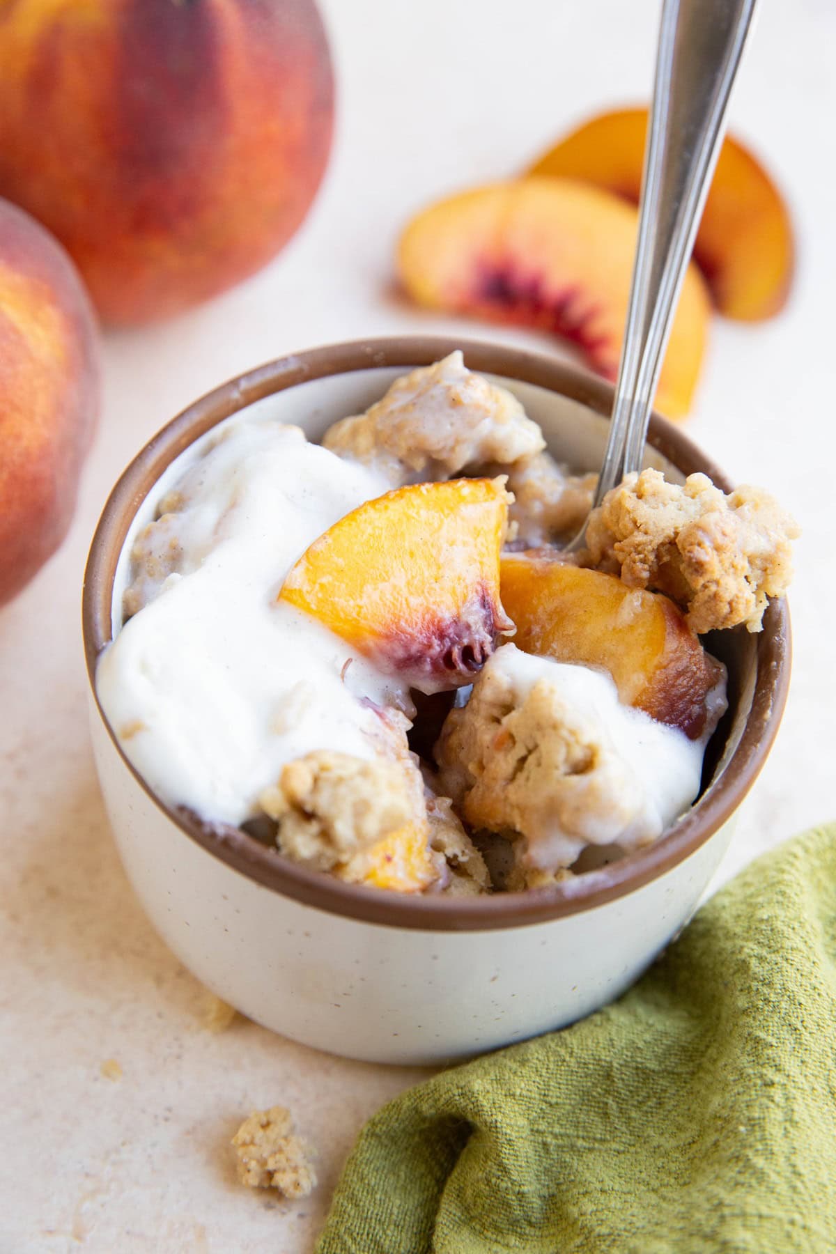 Peach cobbler in a ramekin with melted ice cream and a spoon, ready to serve.