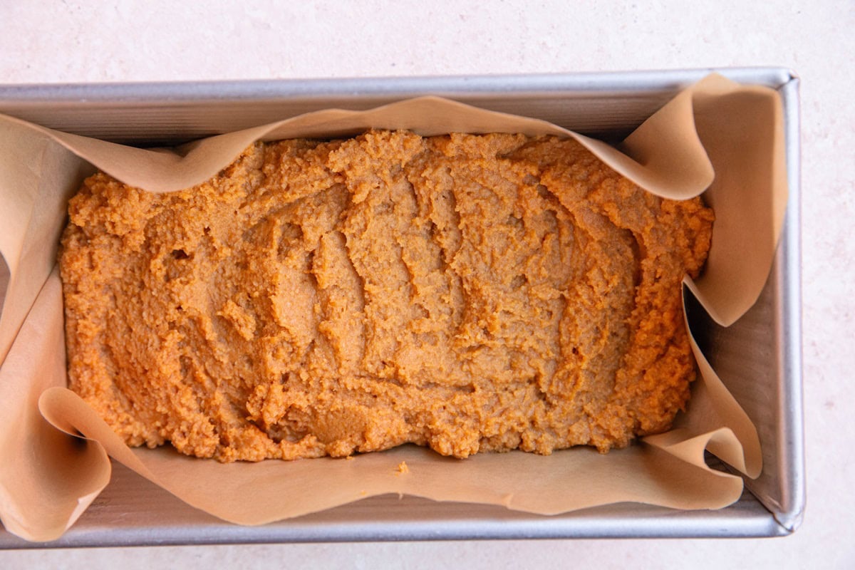 Loaf pan with pumpkin bread batter inside.