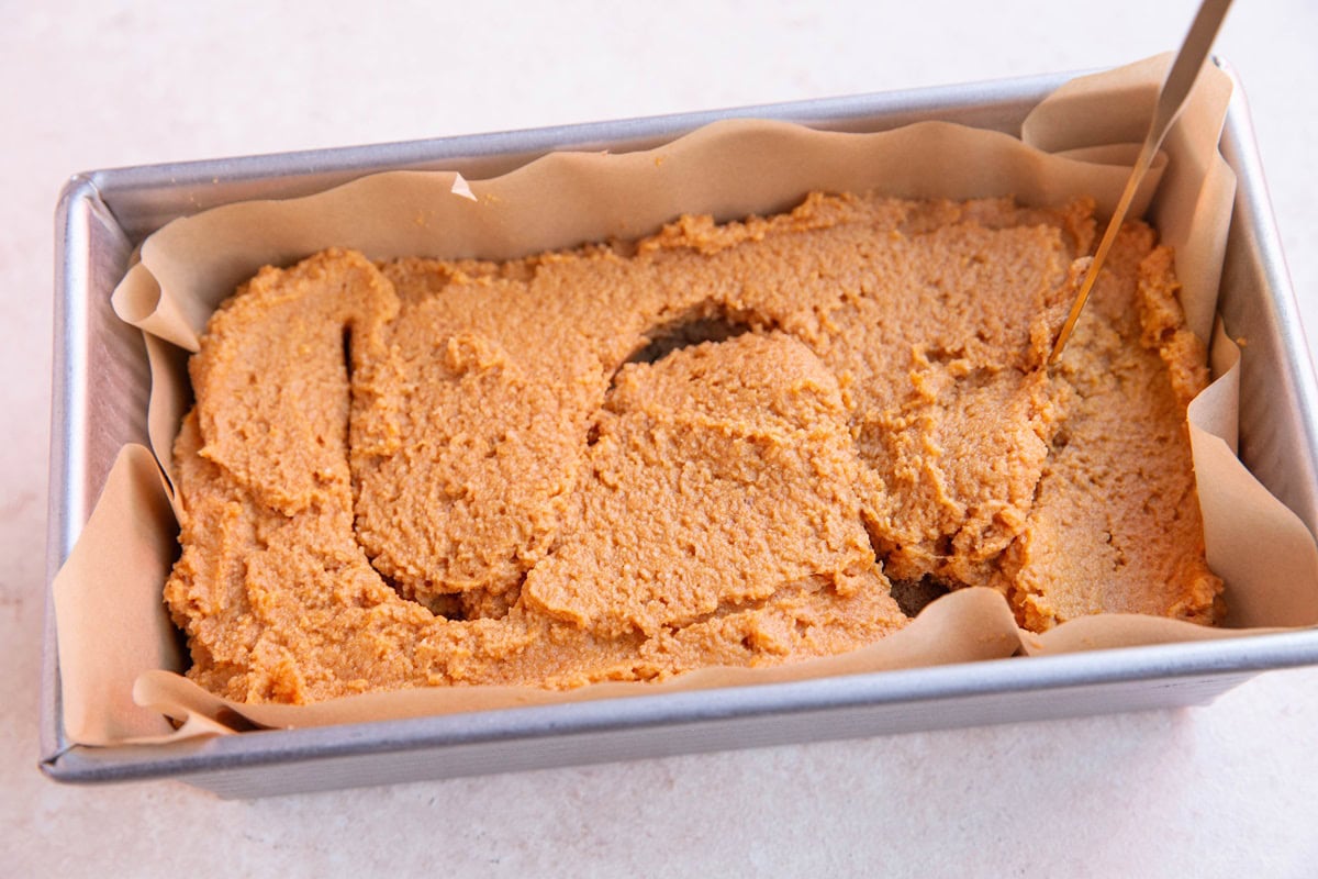 Loaf pan with pumpkin swirl bread batter and a butter knife drawing an S shape into the batter.