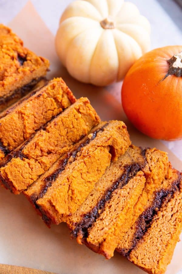 Pumpkin cinnamon swirl bread cut into individual slices with pumpkins in the background.