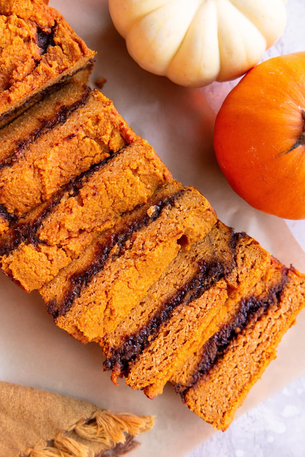 Pumpkin swirl bread on a sheet of parchment paper cut into slices.