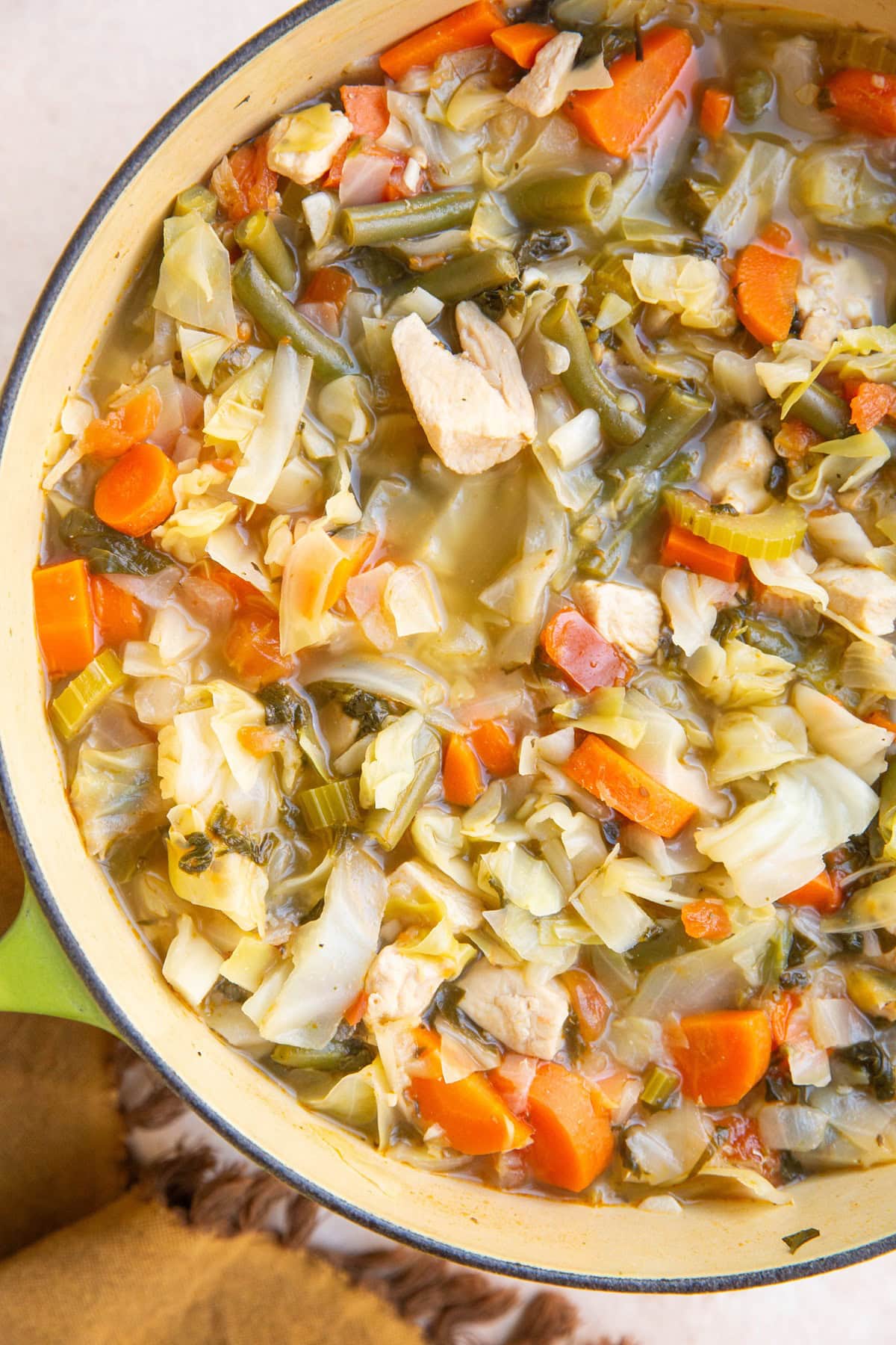 Large Dutch oven full of chicken and cabbage soup with a golden napkin.