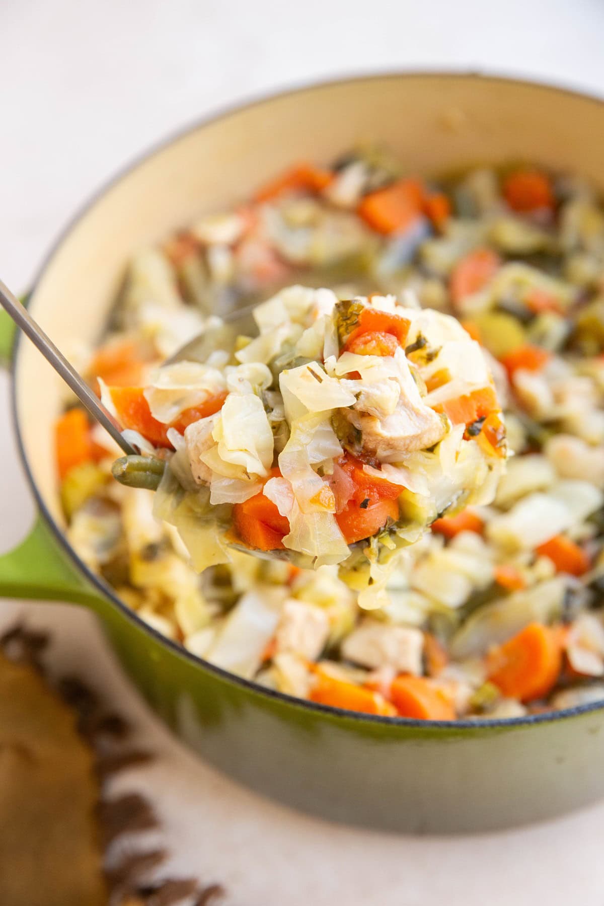 Ladle scooping a big scoop full of chicken and cabbage soup, ready to serve.