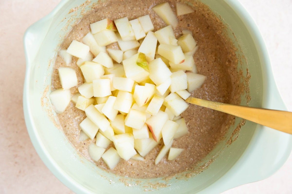 Chunks of apples in a mixing bowl on top of oatmeal bread mixture.